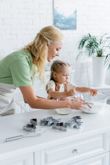 Fototapeta na wymiar girl holding sieve near bowl with flour while helping mom in kitchen