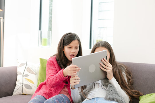 Happy sisters using digital tablet on living room sofa - Powered by Adobe
