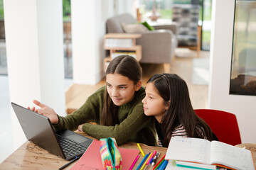 Girl helping young sister with homework on laptop
