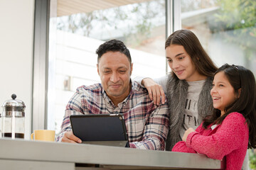 Father and daughters using digital tablet in morning kitchen