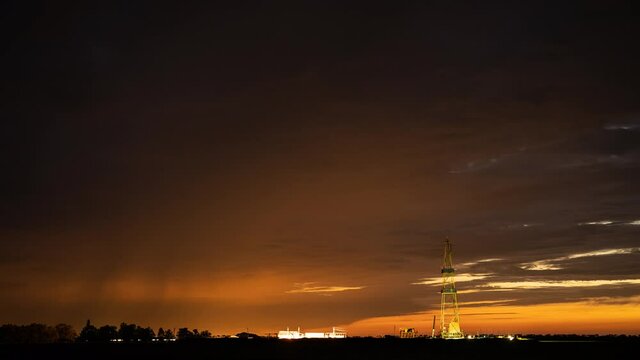 The derrick used for investigation of the gas field in beams of searchlights against the background of the clouds night sky.