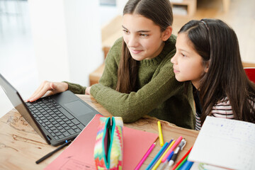 Girl helping young sister with homework on laptop