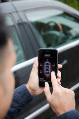 Man setting car alarm from smart phone in driveway