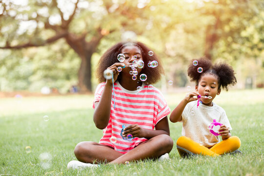 Portrait of group African American curly hairstyle girl playing blowing soap bubbles outdoor. Cute kid girl playing soap bubbles with green nature background in the park - Powered by Adobe