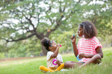 Portrait of group African American curly hairstyle girl playing blowing soap bubbles outdoor. Cute kid girl playing soap bubbles with green nature background in the park