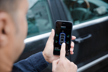 Man setting car alarm from smart phone in driveway