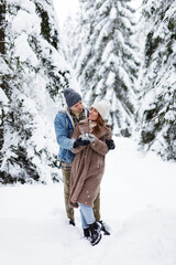 full length portrait of happy couple in winter forest warming up with hot drink