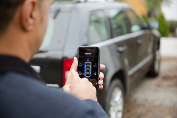 Man setting car alarm from smart phone in driveway