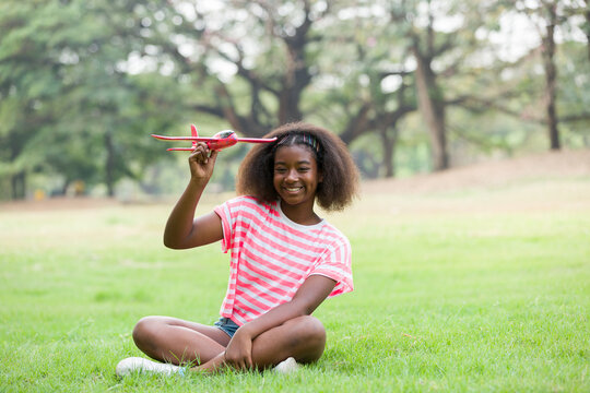 Happy smiling African American girl playing with toy airplane outdoor. Kid having fun with toy airplane in the park. Happy black people. Education and field trips concept