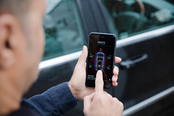 Man setting car alarm from smart phone in driveway