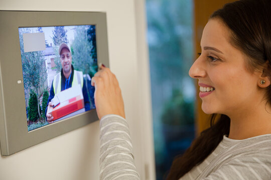 Smiling woman watching deliveryman approaching front door from smart home automation screen