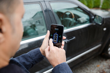 Man setting car alarm from smart phone in driveway