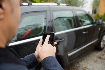 Man setting car alarm from smart phone in driveway