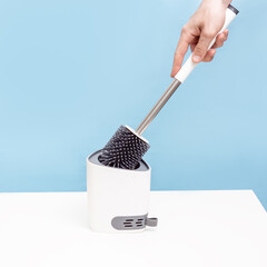 Man holds a silicone toilet brush on blue background. Household cleaning supplies