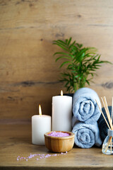 spa and aromatherapy concept-candles, towels, pink sea salt and an aromatic reed diffuser on a wooden table.