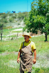 Male farm worker wearing apron and hat looking away standing on field during sunny day