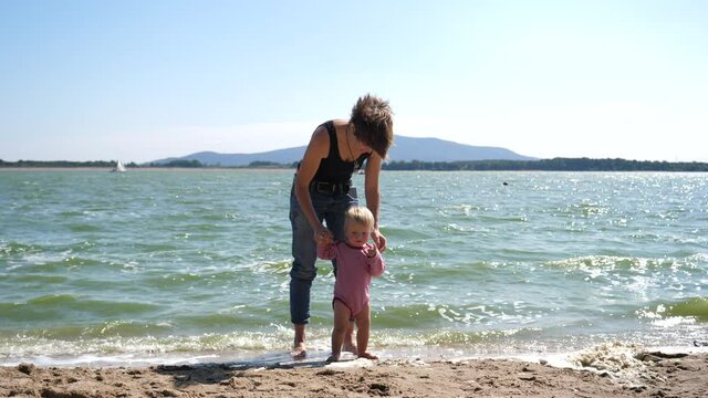 Happy family on a beach mother play with baby toddler son on shallow water sandy lake shore during summer vacation in Poland