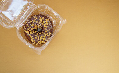 Chocolate donut in a plastic container on a brown or coffee background. Takeaway breakfast concept....
