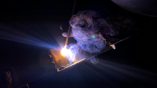 The process of electric welding of metal structures. Bright flames, smoke and sparks. Master in work gloves.