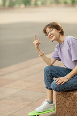 brunette teen girl with glasses with a green skateboard on the streets of the city on a clear sunny day