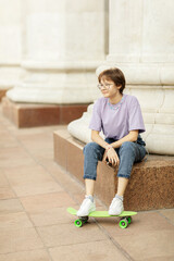 brunette teen girl with glasses with a green skateboard on the streets of the city on a clear sunny day