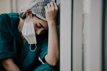 Tired depressed female asian scrub nurse wears face mask blue uniform sits on hospital floor,Young...