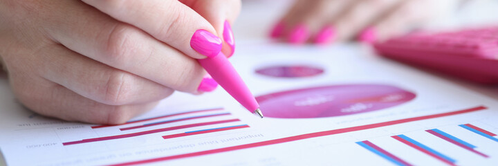 Business woman with pink nails writing with pen in documents with graph closeup