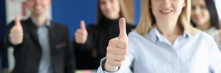 Woman showing thumb up against background of team of colleagues closeup