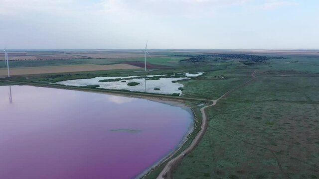 A Wind turbines on the shores of a pink lake at sunset. Lake Lemuria or Pink Lake is a lake in the Kherson region of Ukraine. Aerial view