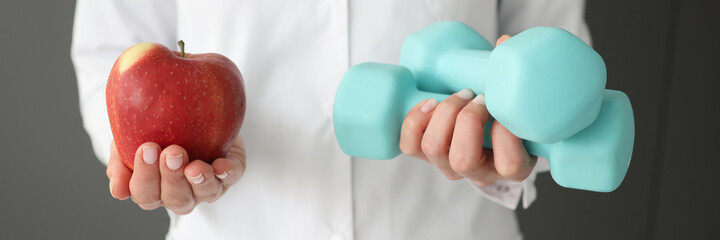 Doctor holding dumbbells and red apple closeup