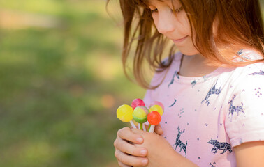 The child holds colorful lollipops in the palms of his hands. Girl with sweets