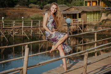 Portrait of a posing smiling blonde girl in a dress in the summer sun