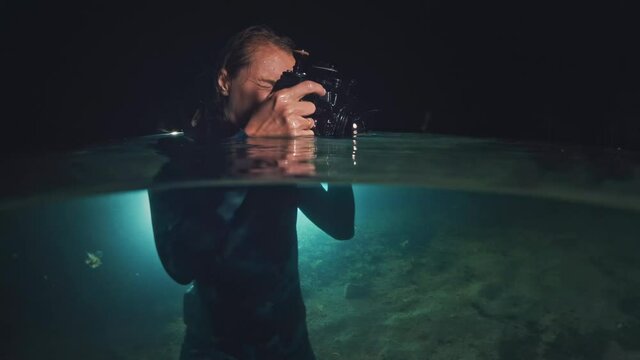 Underwater photographer in night lake. Young woman in wetsuit holds the camera in underwater housing and takes pictures in the lake at night