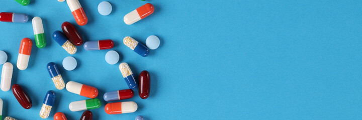 Many multicolored medical capsules and pills lying on blue background