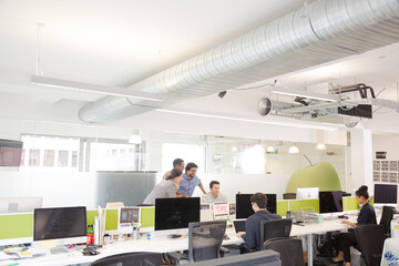 Business people brainstorming at computer in open plan office