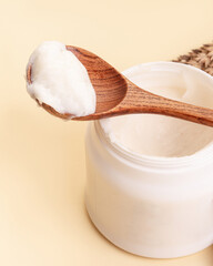 Cream in wooden spoon and plastic jar. Beige background. Beauty concept. Natural cosmetic