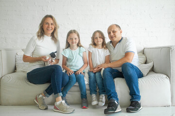 Happy mother and father with little children sitting on sofa and laughing while having fun together at home during weekend