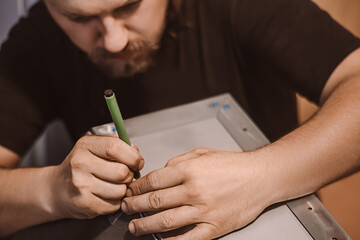 Craftsman mechanic works with metal in workshop. Male worker marks out building structure. Lifestyle, development of small business.