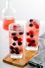 Two tall glasses in front of bottle with cranberry juice