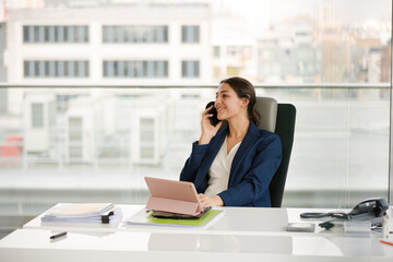 Businesswoman talking on cell phone and using tablet computer at desk