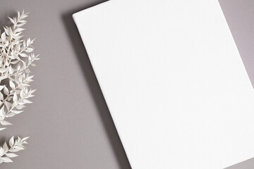 Blank white canvas mockup on gray background with dry plant. Flat lay, top view, copy space