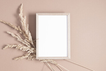 Wooden photo frame mockup with dry plant on beige background. Autumn composition. Flat lay, top view, copy space