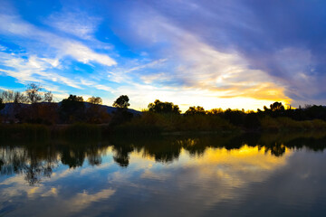Fototapeta na wymiar 茂みのある湖に反射する黄昏空と雲の広がる空