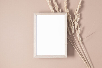 Wooden photo frame mockup with dry plant on beige background. Autumn composition. Flat lay, top...