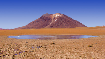 Desolate mountain landscape in the Andes in the north of Chile with volcano and a small frozen lake 