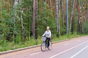Naklejka premium Active senior caucasian woman with gray hair is riding bike on bicycle path in forest park.