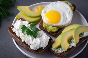 Sandwiches with a minced curd, avocado, fried eggs and herbs on the natural wooden cutting board. Healthy food concept