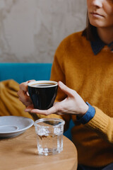  coffee in a beautiful cup, stylish restaurant or coffee shop, cappuccino or Americano for breakfast, meeting of friends or colleagues, orange pillows. a woman's hand holding a cup of black coffee