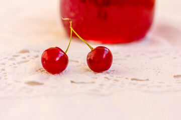 Two cherry berries and a jar of berry jam on white embroidered tablecloth, background. Sour cherry,...