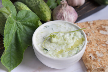 Close-up of tzatziki sauce with pita bread and cucumbers on a wooden board in the background. Mediterranean cuisine